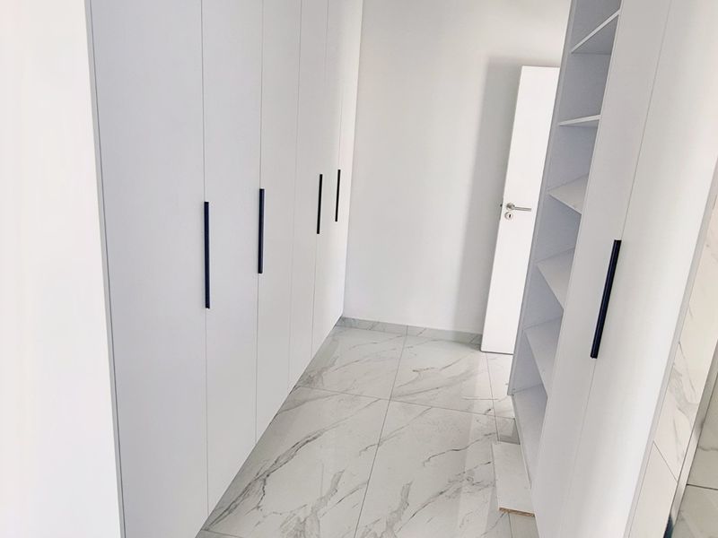 A modern, minimalist dressing area or bedroom space featuring floor-to-ceiling white built-in wardrobes and elegant marble-look tiled flooring.