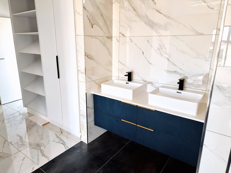 Modern bathroom featuring a sleek double vanity with vessel sinks, matte black fixtures, and elegant marble-look wall tiling with integrated storage shelving.