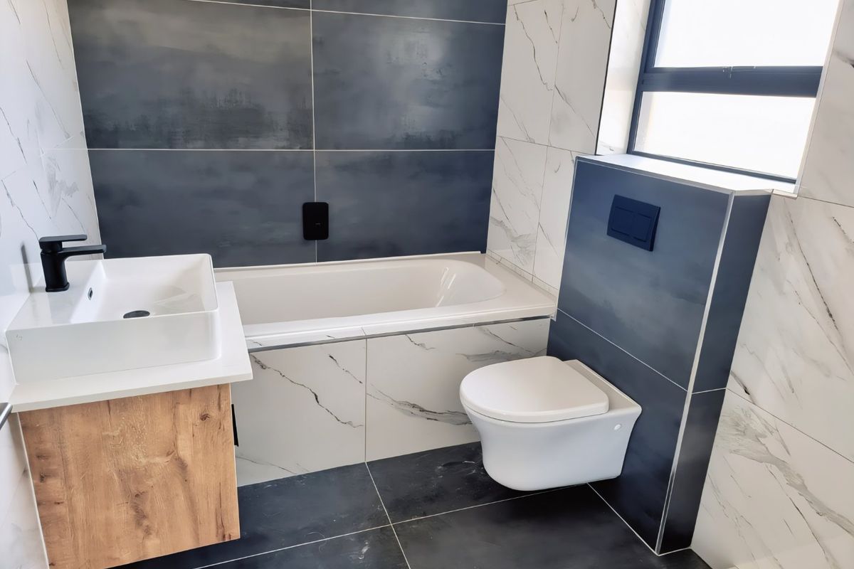 Modern bathroom featuring a wall-mounted toilet with concealed cistern, built-in bathtub, and a contemporary vanity with a countertop basin and black fixtures.