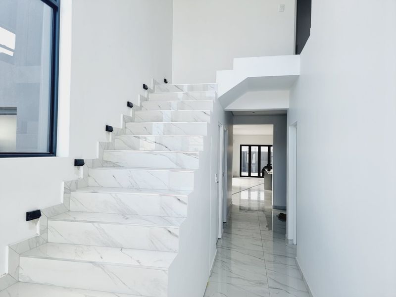 Modern hallway featuring a striking marble-look tiled staircase, matching floor tiles, and clean white walls, leading to an open-plan living area.