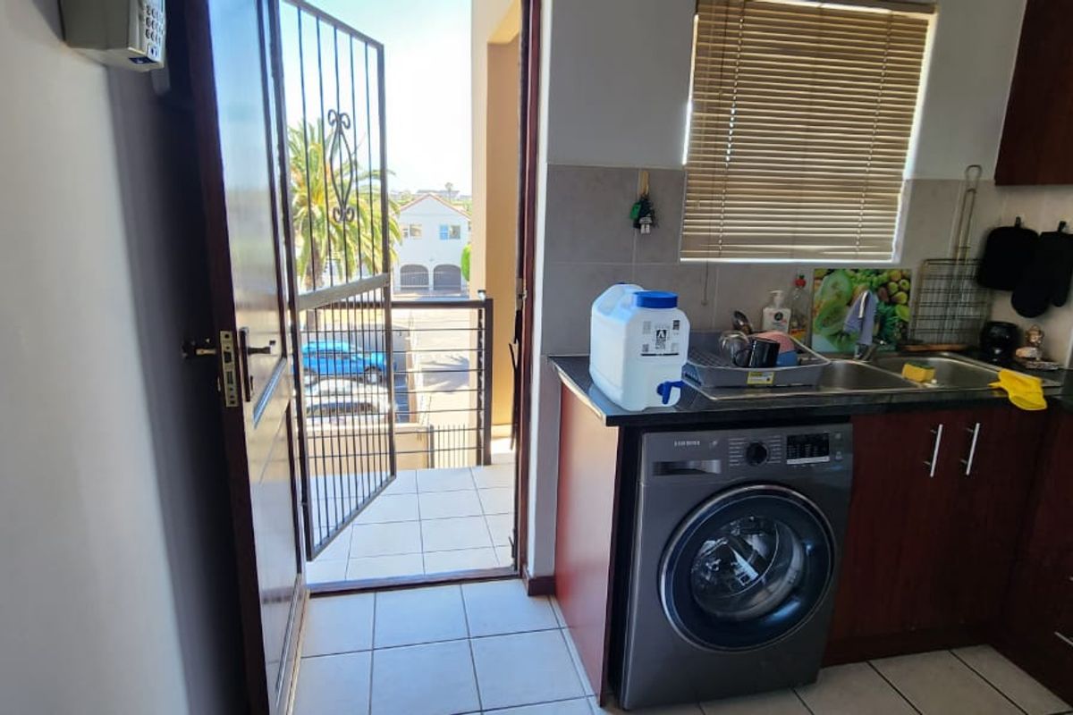 Compact kitchen featuring dark wood cabinetry, granite countertops, tiled flooring, and direct access to an outdoor balcony area.