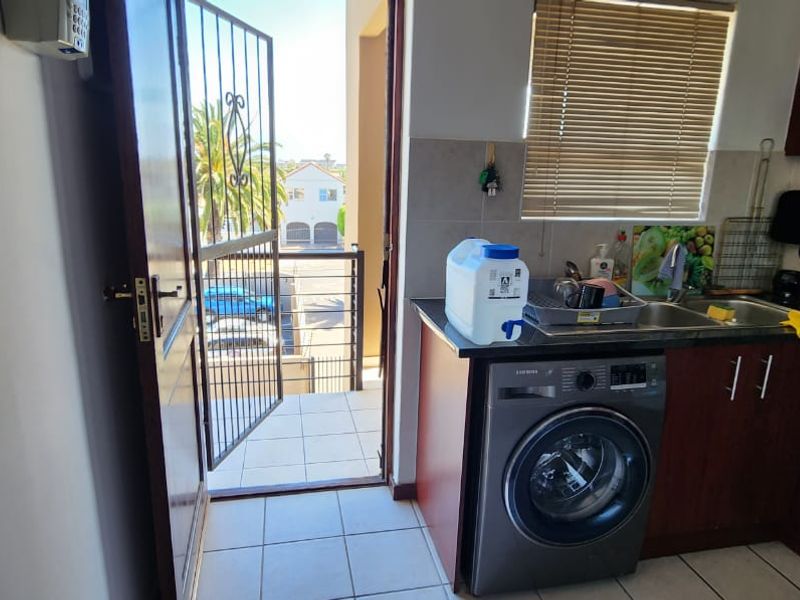 Compact kitchen featuring dark wood cabinetry, granite countertops, tiled flooring, and direct access to an outdoor balcony area.