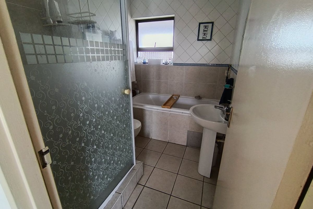A functional bathroom featuring a shower enclosure, a bathtub, and a pedestal sink with tiled finishes throughout.