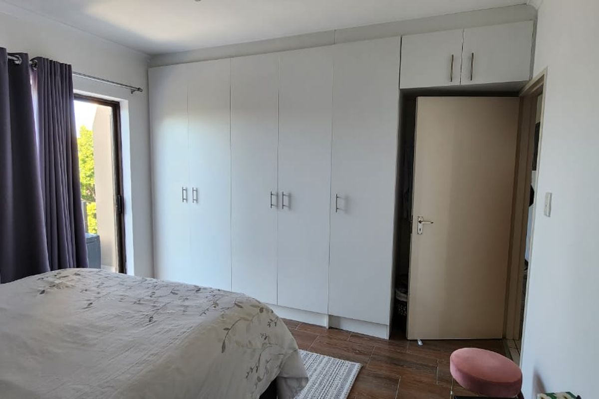 A well-maintained bedroom featuring extensive built-in cupboards, tiled flooring, and direct access to an outdoor balcony through a sliding door.