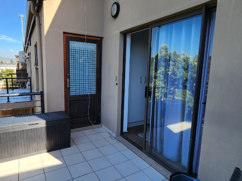 A private balcony featuring tiled flooring, a sliding glass door entrance, and metal safety railings, offering an outdoor extension to the apartment living space.