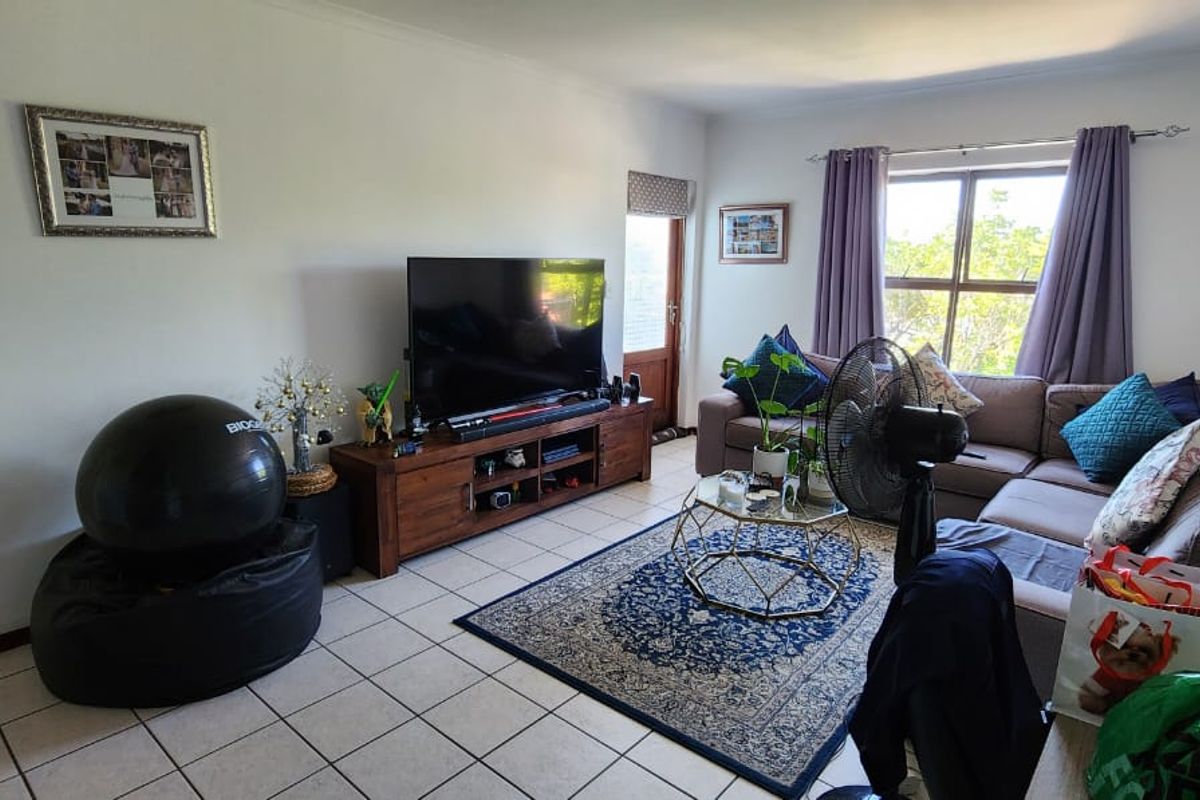 A living room featuring tiled flooring, a large window providing natural light, and a glass panel door leading to an outdoor area.