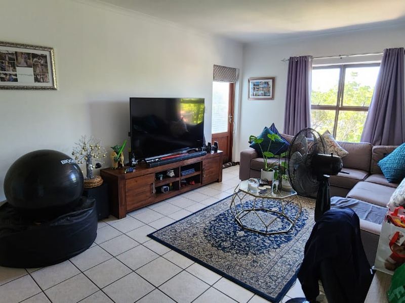 A living room featuring tiled flooring, a large window providing natural light, and a glass panel door leading to an outdoor area.