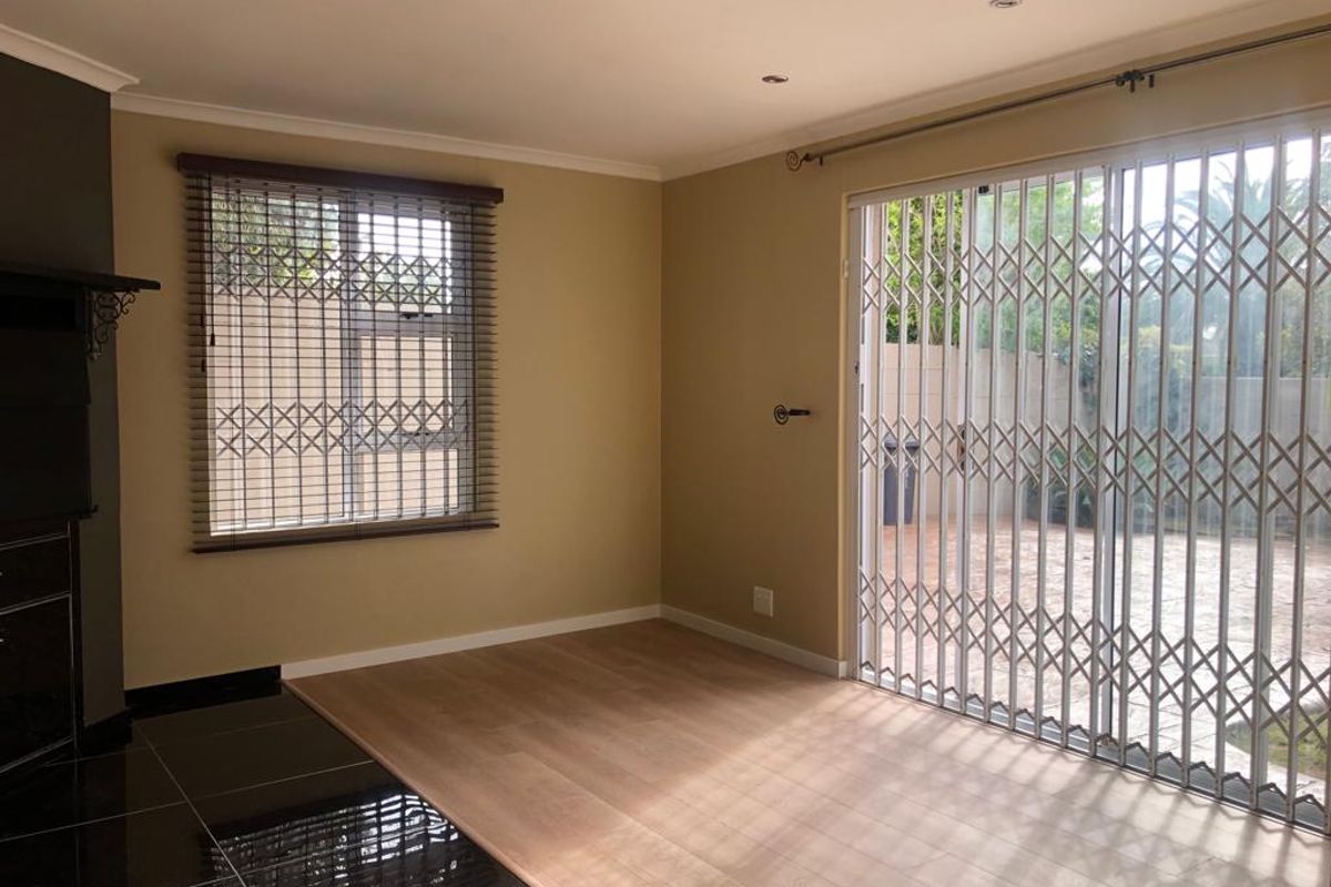 Spacious living area featuring laminate flooring, a black tiled hearth, and large sliding doors with security gates leading to an outdoor patio.