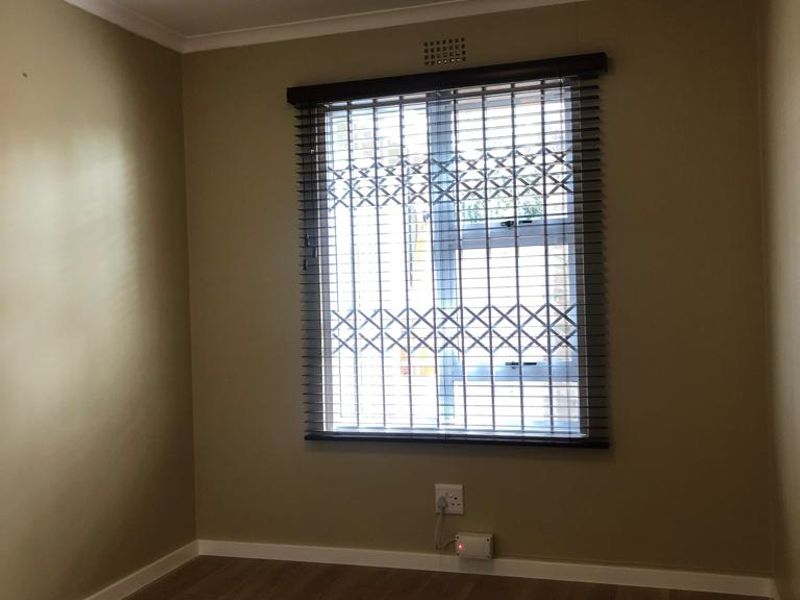 A clean, empty bedroom featuring modern laminate flooring, a secure window with fitted blinds, and neutral wall tones.