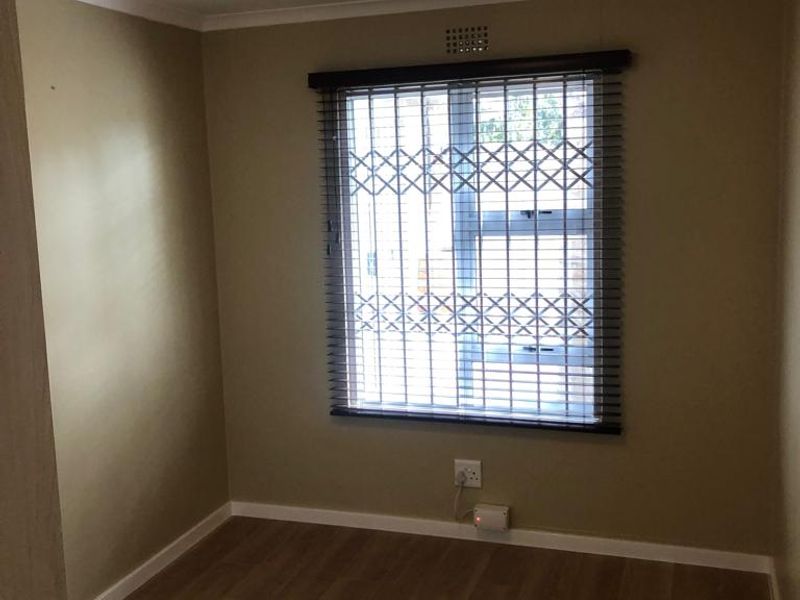A clean, empty bedroom featuring laminate flooring, neutral wall paint, and a window fitted with a security gate.