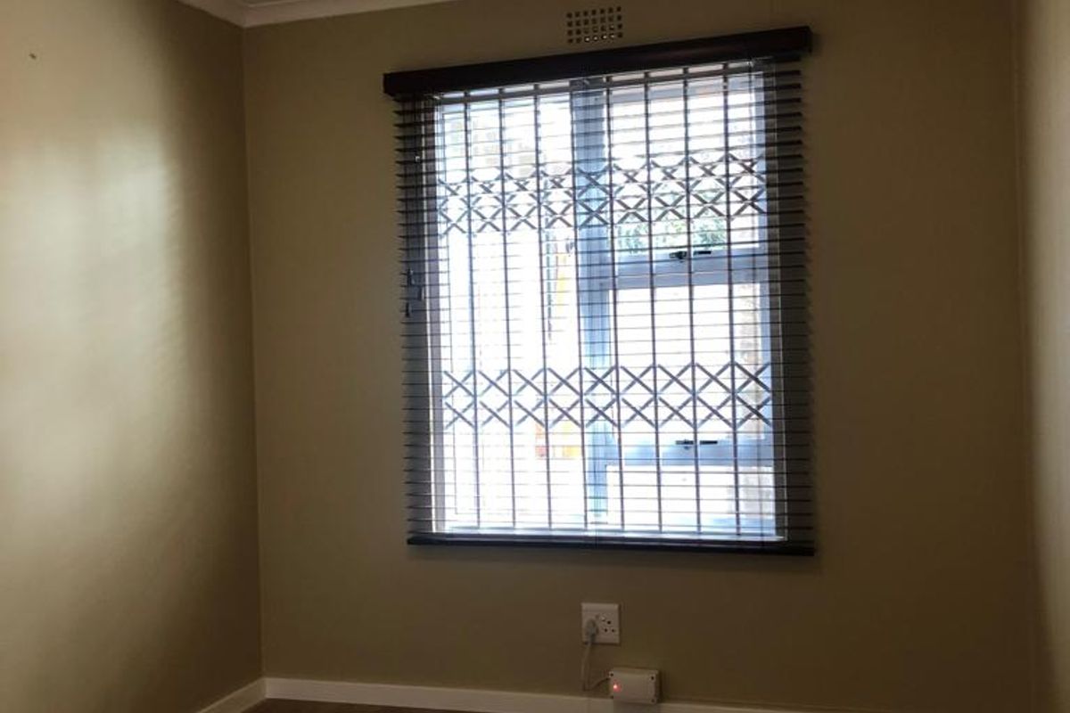 A clean, empty bedroom featuring modern laminate flooring, a secure window with fitted blinds, and neutral wall tones.