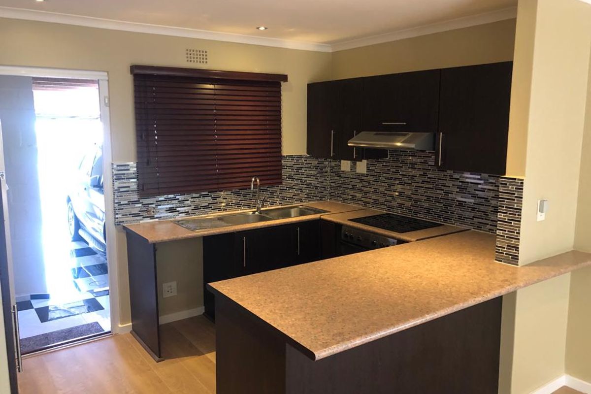 A functional kitchen featuring dark wood cabinetry, laminate countertops, a mosaic tile backsplash, and integrated appliances, including a hob, oven, and extractor fan.