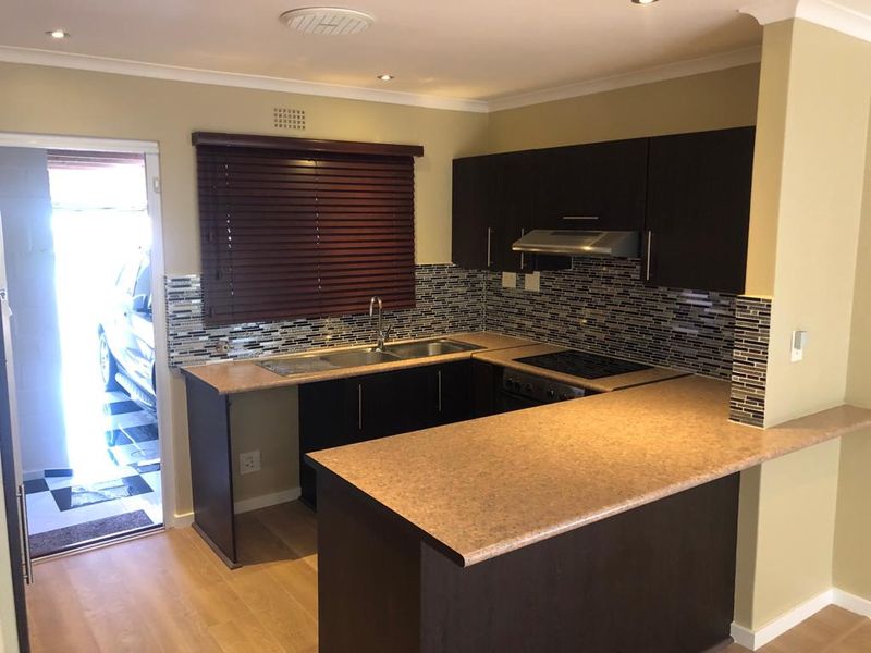 A functional kitchen featuring dark wood cabinetry, laminate countertops, a mosaic tile backsplash, and integrated appliances, including a hob, oven, and extractor fan.