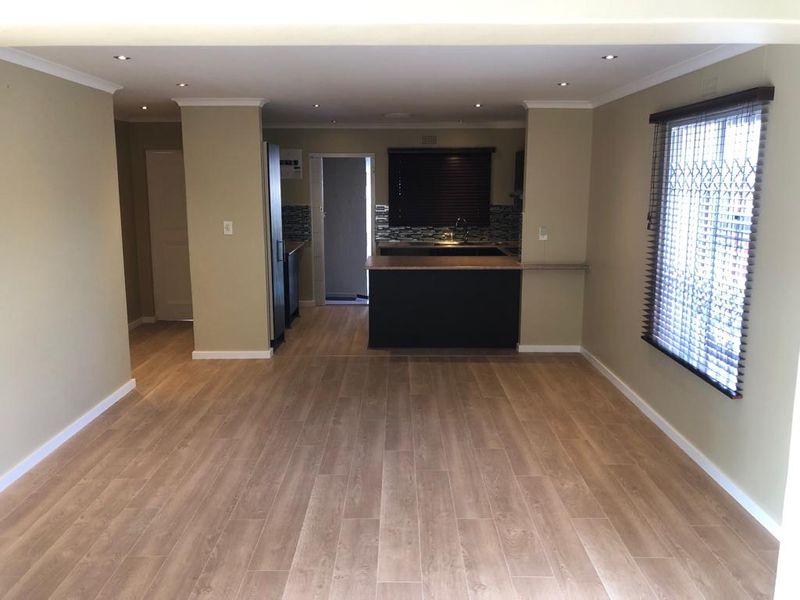 Spacious open-plan living area featuring modern laminate flooring, recessed downlighting, and a functional kitchen with a central island and dark cabinetry.