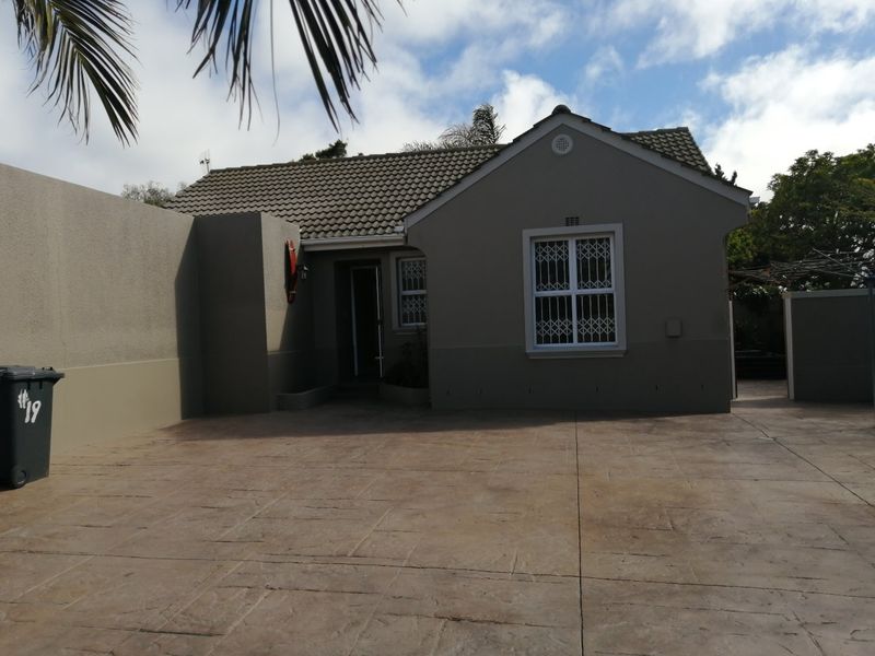 Front elevation of a single-story house featuring a tiled roof, security bars on windows, and a stamped concrete driveway.