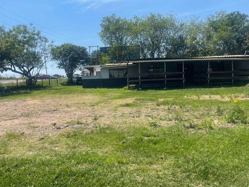 Rear view of a commercial property featuring a covered veranda with timber railing, set on a large grassed lot.