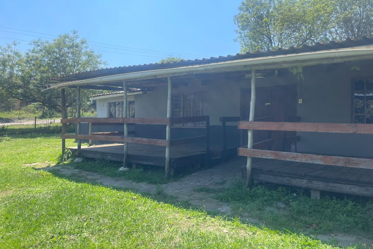 A covered outdoor timber deck area featuring a rustic balustrade and corrugated roof, set against a grassy garden space.