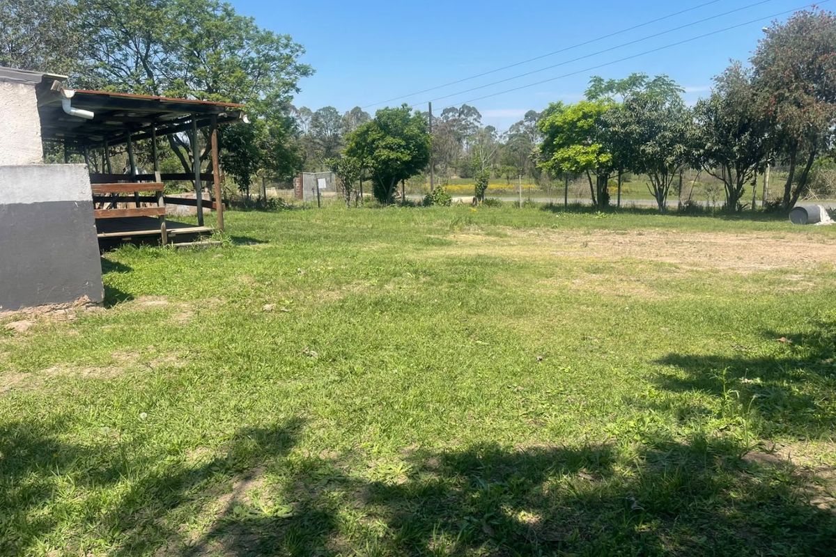 A spacious outdoor garden area featuring a simple covered patio structure and established trees, offering potential for landscaping or outdoor development.
