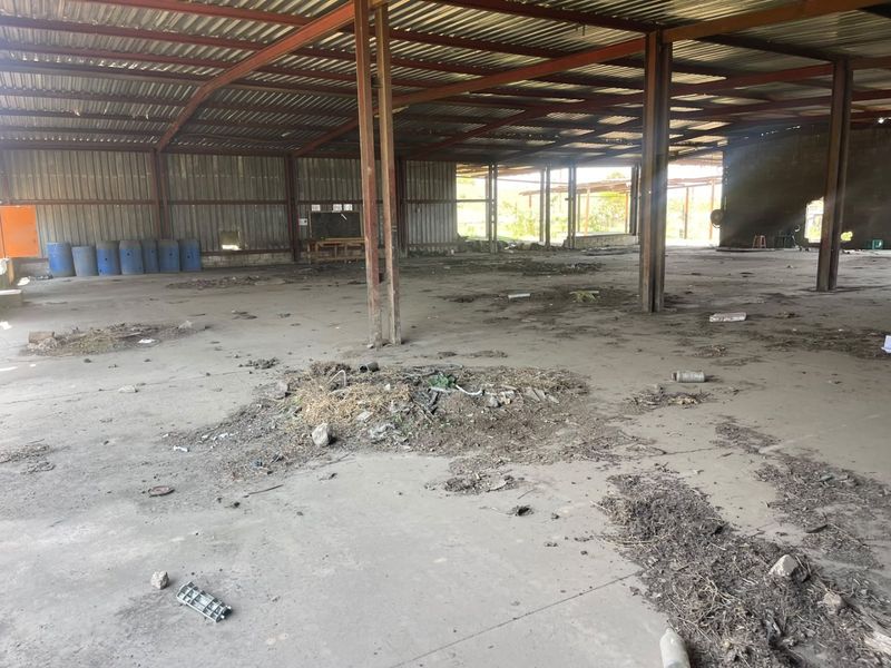 Large open-plan industrial utility space featuring a steel portal frame structure, corrugated metal roofing, and a concrete floor, currently in need of significant maintenance.