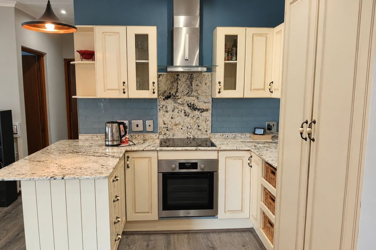 A well-appointed kitchen featuring granite countertops, a built-in oven with extractor fan, subway tile backsplash, and ample cabinetry with a dedicated pantry unit.