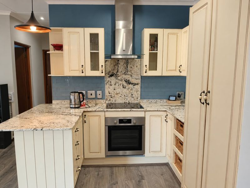 A well-appointed kitchen featuring granite countertops, a built-in oven with extractor fan, subway tile backsplash, and ample cabinetry with a dedicated pantry unit.