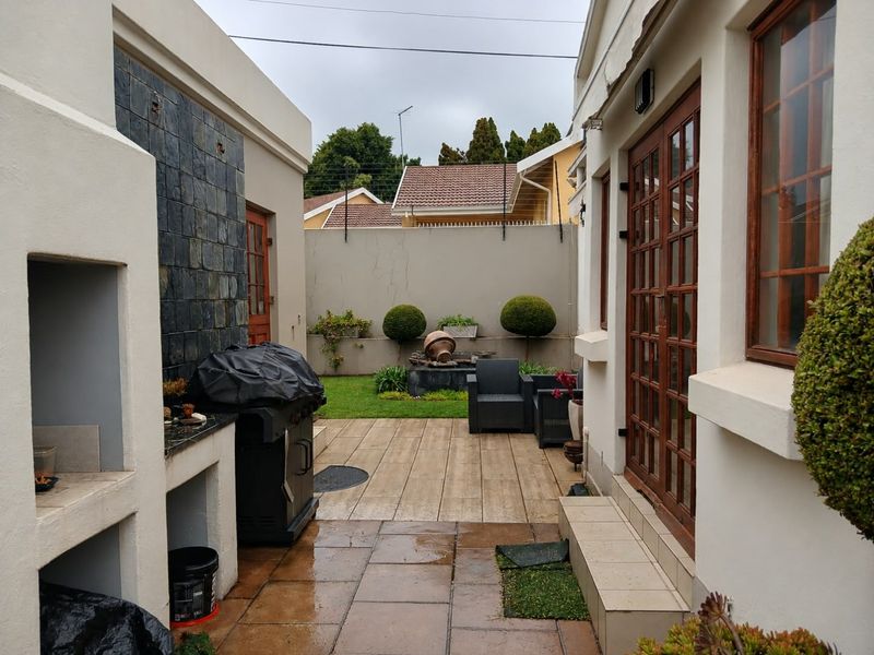 A paved outdoor patio area featuring a built-in braai, stone cladding, and direct access to the home through wooden framed glass doors.