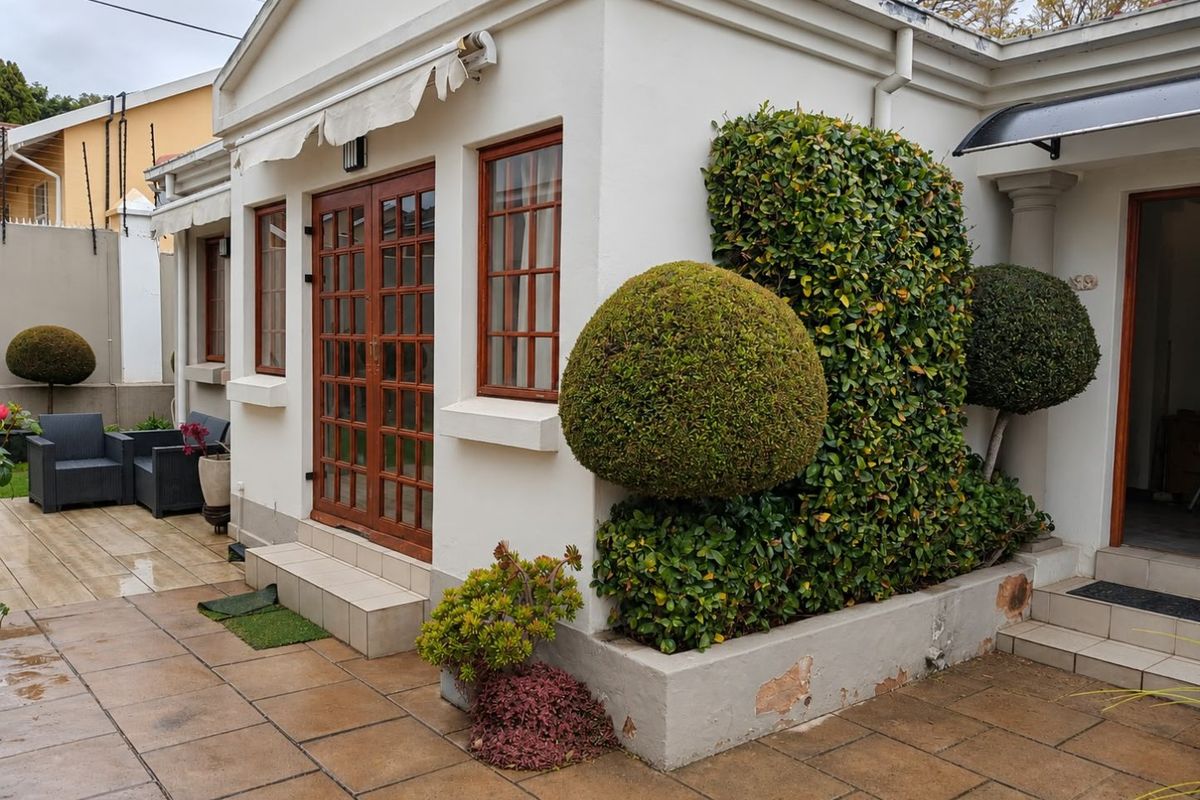 A rear exterior view featuring a tiled patio, timber-framed french doors, a retractable awning, and a landscaped masonry planter box.