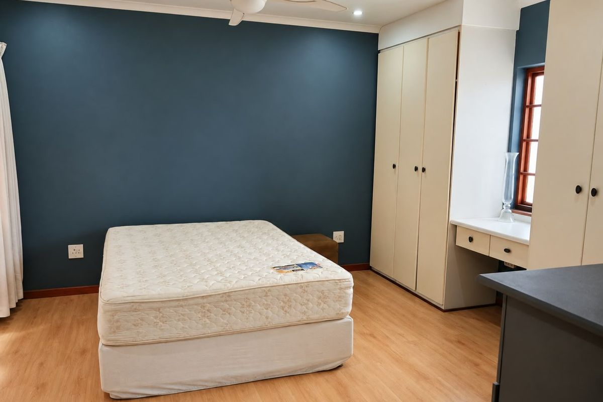 Spacious bedroom featuring laminate flooring, built-in cupboards with an integrated vanity, and a ceiling fan.