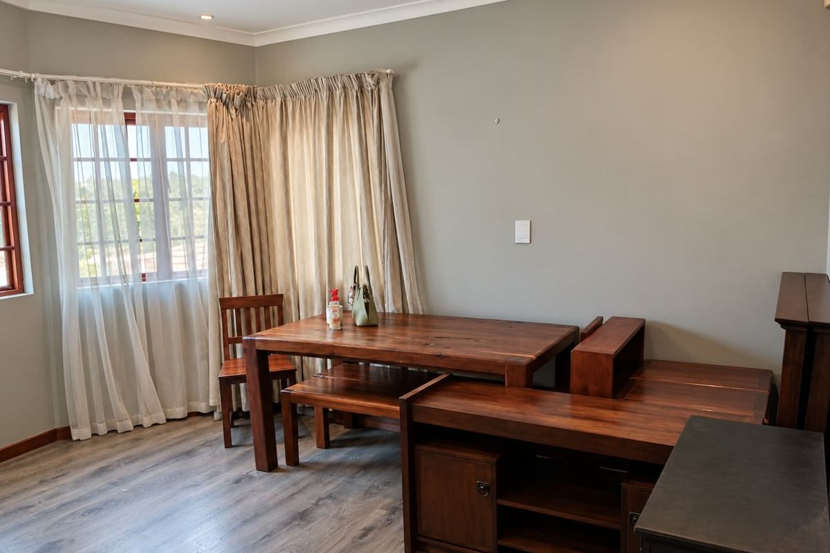 A living area featuring modern laminate flooring, neutral wall tones, and natural light through window frames with fitted curtain tracks.