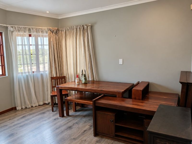 A living area featuring modern laminate flooring, neutral wall tones, and natural light through window frames with fitted curtain tracks.