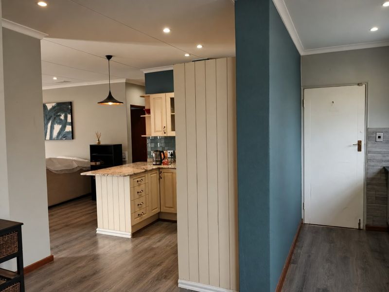 An open-plan living and kitchen area featuring modern laminate flooring, granite countertops, and a neutral color palette with a striking blue accent wall.