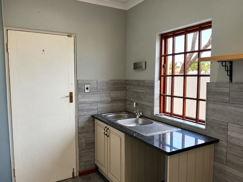 A clean and functional scullery area featuring a double stainless steel sink, granite countertops, and modern grey tiled splashbacks with a timber-framed window.