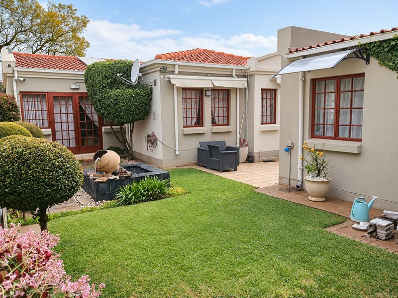 A well-maintained rear garden featuring a paved patio area, a water feature, and classic timber-framed windows and doors under a terracotta tiled roof.