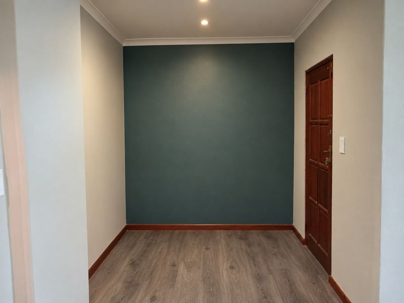 A clean and well-maintained entrance area featuring modern laminate flooring, a feature wall, and recessed downlighting.