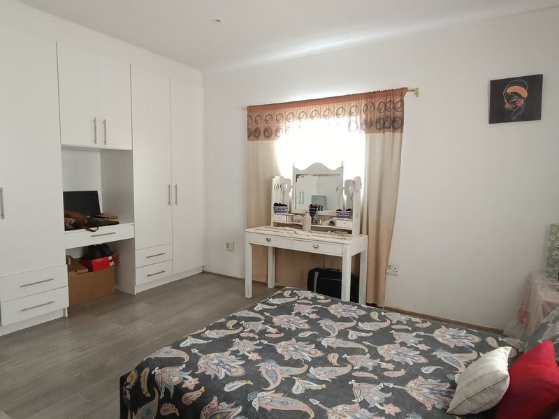 A well-maintained bedroom featuring extensive built-in cupboards, a dedicated desk area, and modern laminate flooring, offering a clean and functional living space.