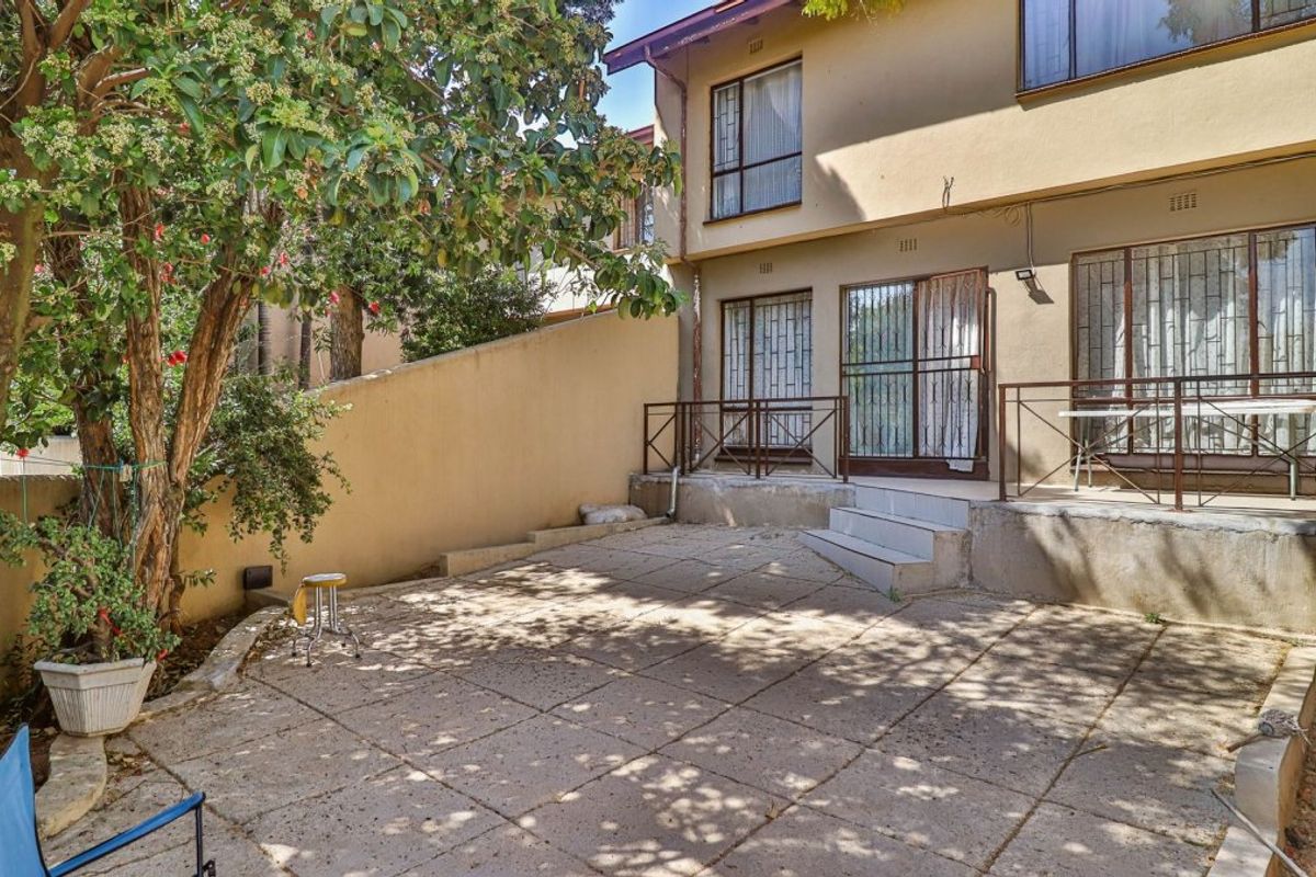 Rear exterior view of the apartment featuring a paved patio area, retaining wall, and metal security gates leading into the living space.