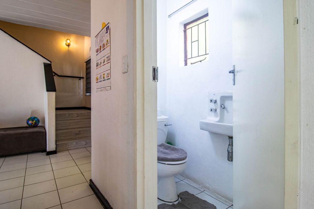 A compact bathroom featuring a standard toilet and wall-mounted basin, situated adjacent to a tiled hallway area.
