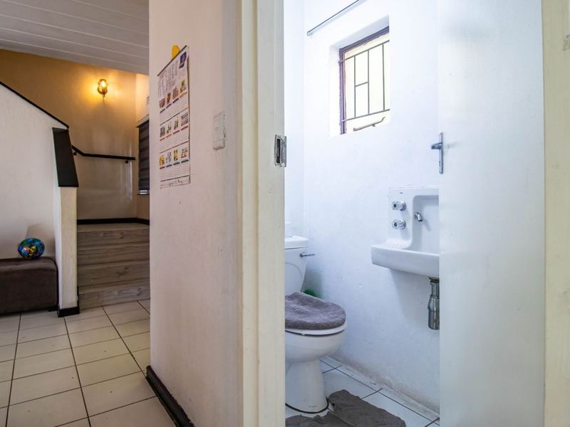 A compact bathroom featuring a standard toilet and wall-mounted basin, situated adjacent to a tiled hallway area.