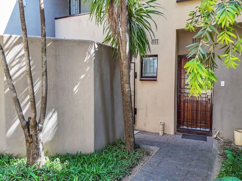 Front entrance of the apartment featuring a paved walkway, security gate, and exterior wall lighting.
