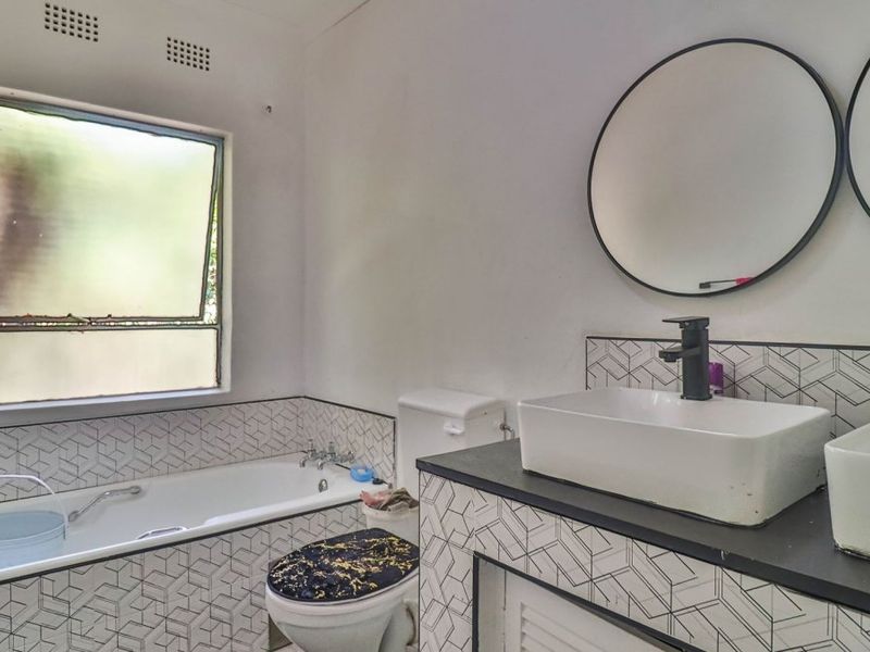 A functional bathroom featuring dual vessel sinks with modern black faucets, a built-in bathtub, and distinctive geometric wall tiling.