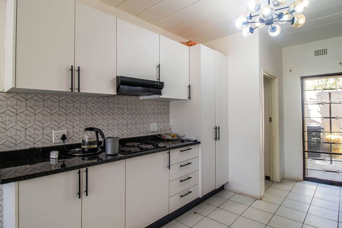 A functional kitchen featuring white cabinetry, granite countertops, an electric hob with extractor fan, and a tiled backsplash, leading to an exterior security door.