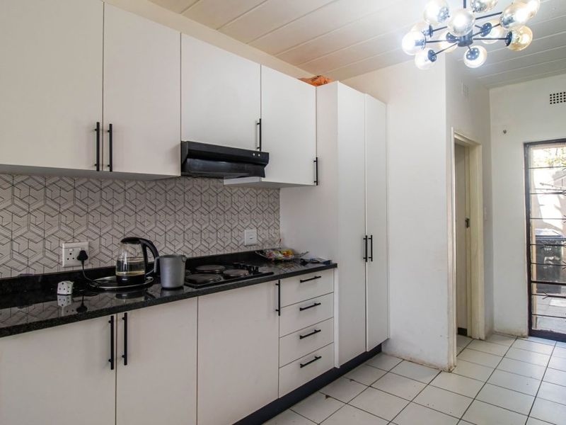 A functional kitchen featuring white cabinetry, granite countertops, an electric hob with extractor fan, and a tiled backsplash, leading to an exterior security door.