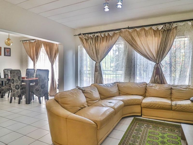Spacious open-plan living and dining area featuring tiled flooring and large windows with security bars, offering a functional layout for family living.