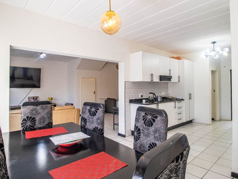 Open-plan living and dining area featuring a functional kitchen with built-in cabinetry, hob, and extractor fan, finished with tiled flooring throughout.