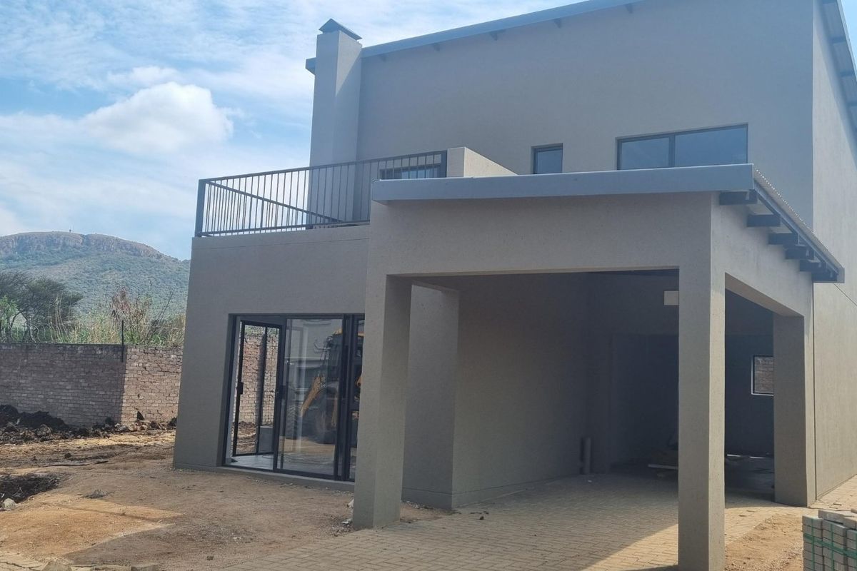Rear view of a modern townhouse featuring a covered patio, paved driveway, and an upper-level balcony with metal railings.