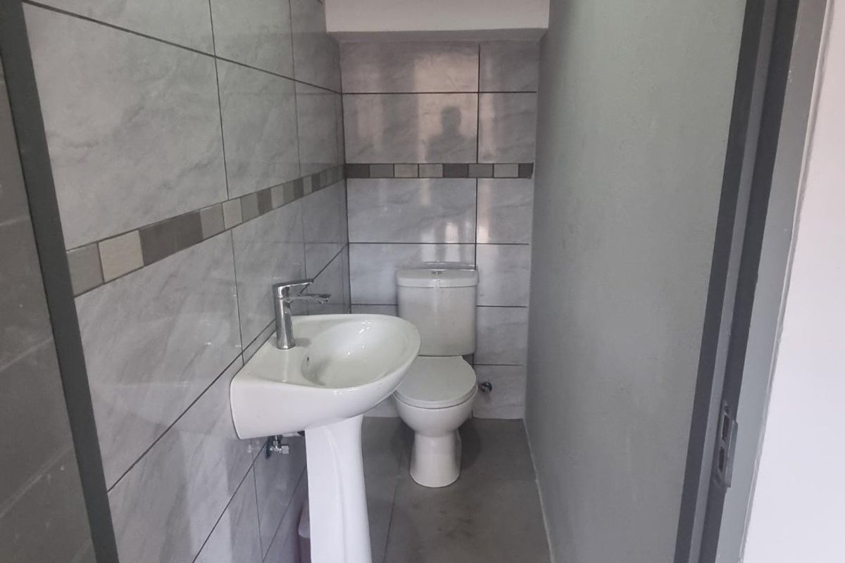 A compact guest bathroom featuring modern grey ceramic wall and floor tiles, a pedestal washbasin, and a standard toilet.