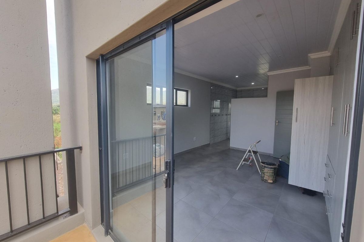 A modern, empty bedroom featuring large sliding glass doors leading to a balcony, tiled floors, and built-in cabinetry.