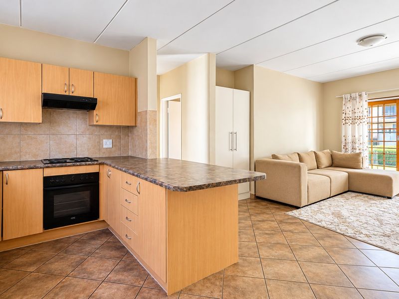 Open-plan kitchen and living area featuring laminate cabinetry, built-in appliances, tiled flooring, and direct access to an outdoor patio through sliding glass doors.