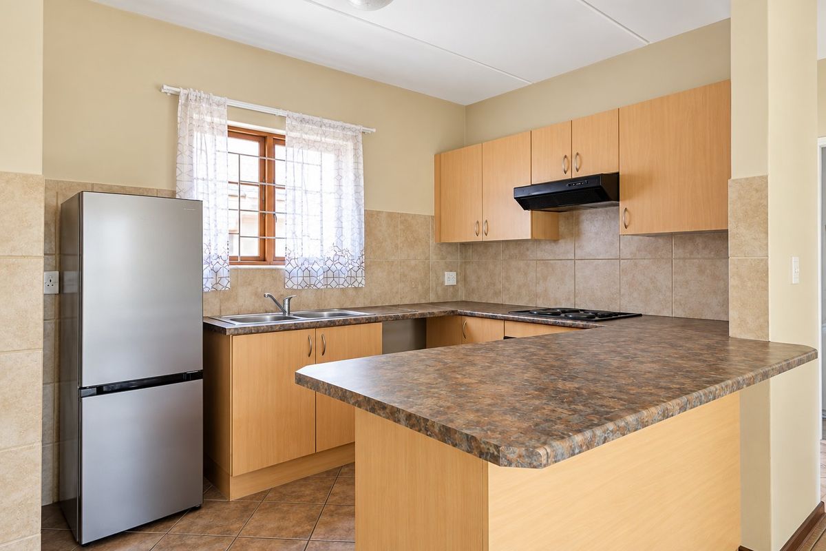 A functional kitchen featuring light wood-finish cabinetry, laminate countertops, a built-in hob with extractor fan, and neutral ceramic tile backsplash and flooring.
