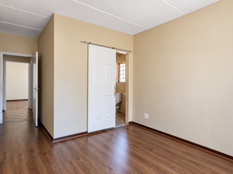 An empty bedroom featuring laminate flooring, a sliding barn door leading to an en-suite bathroom, and neutral wall finishes.